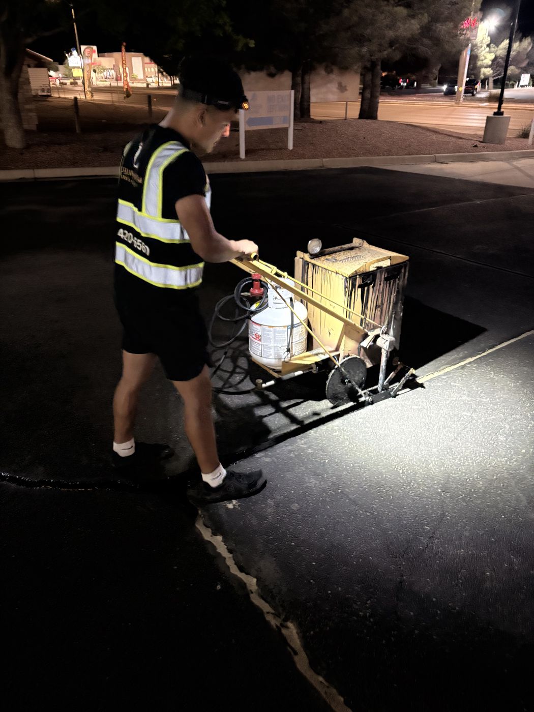 Lujan's Line crew member hot-pour crack filling a parking lot at night